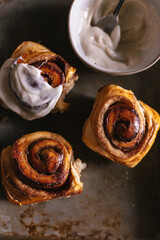 Baked cinnamon bun rolls with white vanilla bean cream frosting. Moody dark food photo. Closeup flat lay. Baking tray. Baked pastry breakfast. Fresh baking treat. Brown cinnamon sugar. Swirls on roll