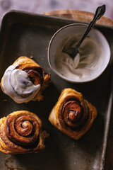 Baked cinnamon bun rolls with white vanilla bean cream frosting. Moody dark food photo. Closeup flat lay. Baking tray. Baked pastry breakfast. Fresh baking treat. Brown cinnamon sugar. Swirls on roll