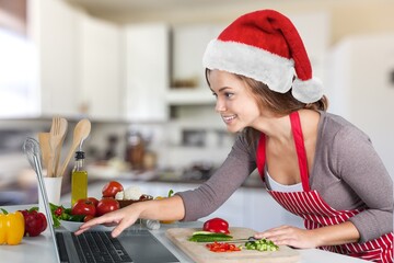Smiling girl wearing Santa hat having video calling family by webcam. Woman with laptop sitting on kitchen