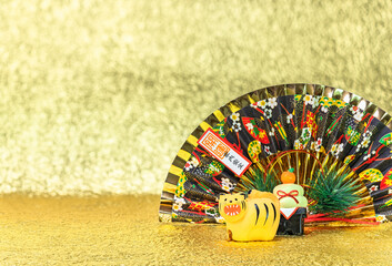 Japanese New Year's Greeting Card of a funny roaring tiger figurine for the year 2022 with a folding fan written good luck for a safe house against a gold background.