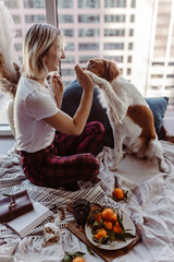 Woman and dog cuddle on bed. Winter cozy vibes. Mandarins, lights, books. Cute puppy. Brittany breed. Merry Christmas time. Holiday festive season.Cold winters.Staying at home.Warm blanket and pillows