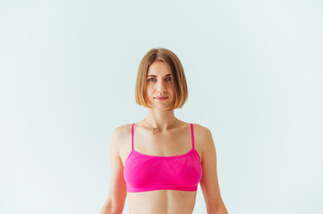 Fototapeta premium Portrait of a beautiful athletic woman trainer on a white background in a pink top, looking at the camera with a slight smile on his face.