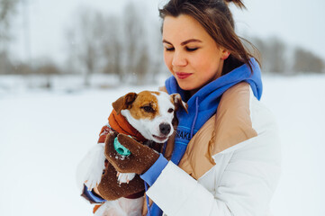 Naklejka na ściany i meble Portrait of a beautiful woman with a cute little dog on a walk in the cold season on a background of snowy views.