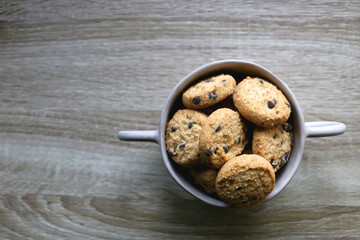 Ceramic bowl filled with chocolate chip cookies on wooden table. Flat lay.