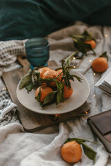 Cozy winter vibes. Christmas lights, mandarins, book. In bed. Christmas holiday. Flat lay moody photo. Cozy comfort bed near window. Pillows, blanket. Orange fruits, ornaments. Soft warm tones.