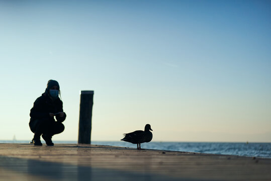 female tourist wearing a mask making a photo of a duck in lago di garda 