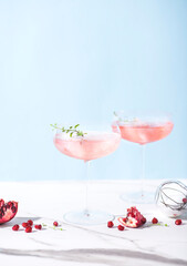 Winter holidays festive alcohol pink cocktails with peace of pomegranate in the marble table, winter drink concept, front view, vertical format