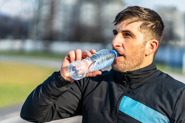 close up portrait of adult caucasian man standing outdoor with plastic bottle of water drinking -...
