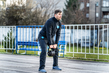 Portrait of one adult caucasian man male athlete standing outdoor at stadium track hold kettlebell in hand doing swing - strength and endurance training concept in spring or autumn day copy space