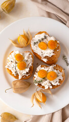 Top view of Ricotta Crostini topped with cape gooseberries on a white plate. Ripe fresh Physalis plant, yellow berry. Tropical fruit and food for health concept.