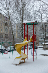 Snow-covered children's slide in the courtyard of a residential area