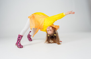 Portrait of a beautiful little girl in a yellow raincoat standing upside down on an isolated white...