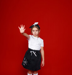 Portrait of a beautiful little girl posing on an isolated red background. extend your arm forward stop