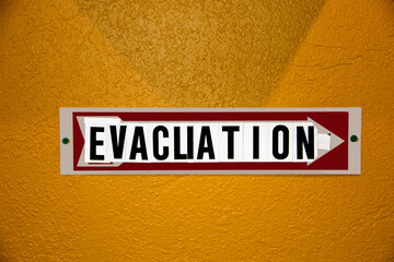 Evacuation Sign- hobbled together from some other kind of sign and stick on letters - tacked to orange stucco wall.