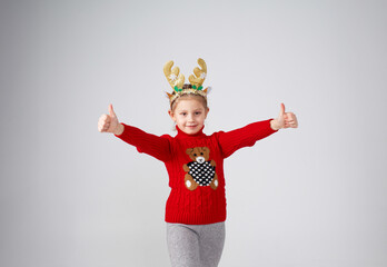 a little girl in a red pullover deer antlers on her head thumbs up joy positive on an isolated white background. Christmas.