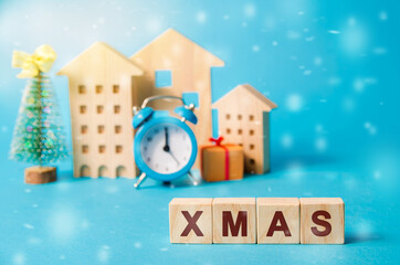 Wooden blocks with the word Xmas, miniature houses, clock and a Christmas tree. New Years celebration concept. Holiday sales and promotions. Merry christmas and happy new year