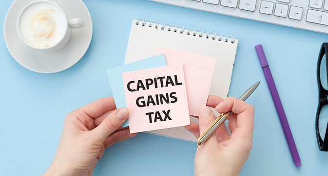 Closeup on businessman holding a card with text CAPITAL GAINS TAX, business concept image with soft focus background and vintage tone