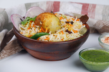 Egg biryani with a fried egg in a wooden bowl with green coriander chutney and raita 