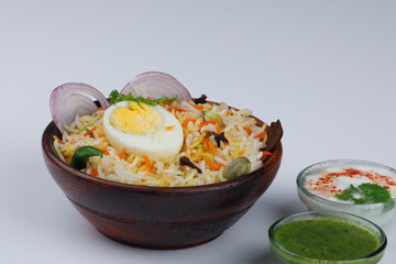 Fresh Egg biryani with a half-cut boiled egg served in a wooden bowl with green coriander chutney and raita isolated on white background