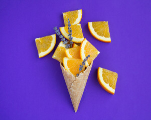 Ice cream cone with chopped orange fruit and lavender flower on the purple background. Top view....