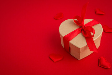 Beautiful minimal wrapped gift box heart shaped with red bow ribbon on red background and small padded hearts top view flat lay, present for Saint Valentine day, love and relationship, space for text
