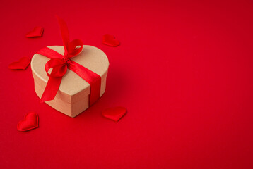 Beautiful minimal wrapped gift box heart shaped with red bow ribbon on red background and small padded hearts top view flat lay, present for Saint Valentine day, love and relationship, space for text