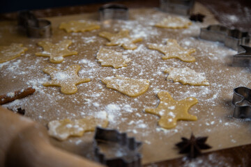 There are ready-made cookies of different shapes on the parchment, a rolling pin, cookie cutters and a sieve with flour are lying nearby, flour is scattered everywhere. High quality photo