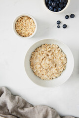 Bowl of porridge, bowl of blueberries and a bowl of oats on white marble countertop