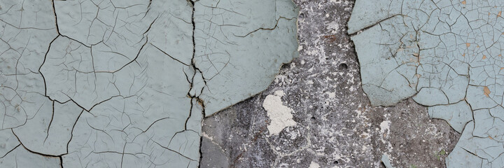 Peeling paint on the wall. Panorama of a concrete wall with old cracked flaking paint. Weathered rough painted surface with patterns of cracks and peeling. Wide panoramic grunge texture for background