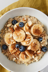 Bowl of porridge topped with banana, blueberries, almonds and cinnamon on a green linen