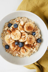 Bowl of porridge topped with banana, blueberries, almonds and cinnamon on a green linen