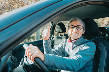 Portrait of a happy smiling senior woman learning to drive a car holding the car key to...