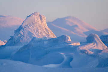 Winter arctic landscape. Ice hummocks and snowdrifts against the background of blurred mountains....