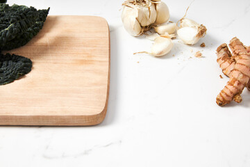 Dinasour kale on a cutting board with garlic and turmeric root placed on a marble countertop