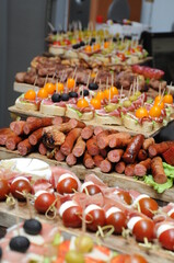 Grilled meat and sausages served on a wooden board. Decorative food is served in the background