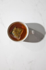 Top view of one white mug with herbal tea and tea bag