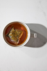 Top view of one white mug with herbal tea and tea bag