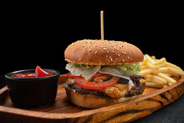 Burger with meat tomatoes and cheese, french fries and sauce, on a black background