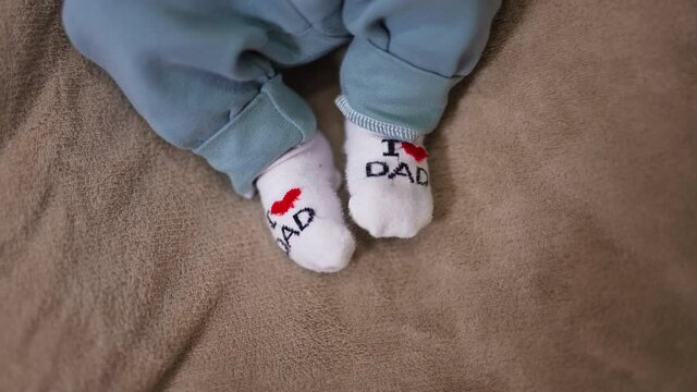 Adorable babe’s feet in tiny socks. I love you dad socks on the little feet on the grey backdrop. Close up.