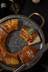 King porcelain figurine stands over a half Roscón de Reyes piece next to a serrated bread knife.