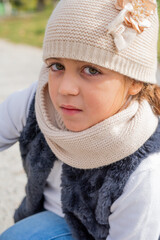 Close-up portrait of a Caucasian girl with cap and scarf on a sunny day.