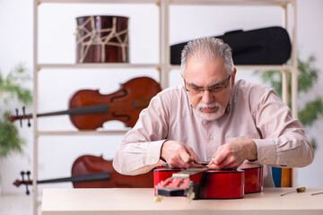 Old male repairman repairing musical instruments at workplace