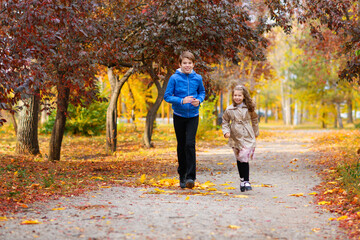 Fototapeta premium children run along the path in the autumn park . they play and laugh, they have a lot of fun. they are surrounded by beautiful nature and trees with yellow and red leaves