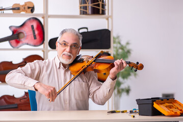 Old male repairman repairing musical instruments at workplace