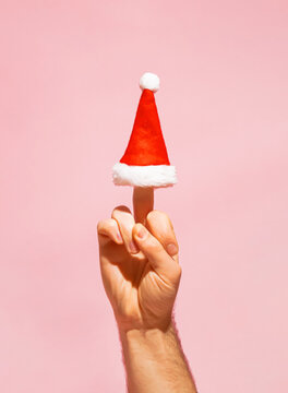 Hand shows aggresive gesture with the middle finger and Santa Claus hat. Fuck you concept. Minimal New Year idea.
