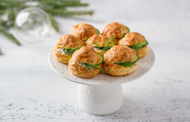 Cheese profiteroles with cream cheese, cucumber and herbs, gougeres, traditional French pastries, in white plate on a light gray background, top view. Delicious snack for New Year's table or buffet