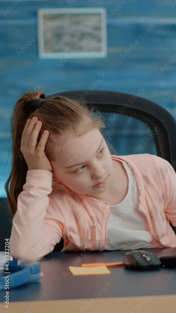 Poster exhausted child looking at computer for online classes while sitting at desk. little girl feeling ti