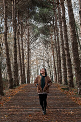 Beautiful girl walking in nature, looking up. Girl in autumn clothes. Outdoor portrait of alone, beautiful, young girl walking in autumn forest. Full length photo.
