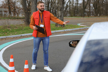 Instructor near car with his student during exam at driving school test track