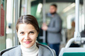 Portrait of smiling brunette wearing stylish light overcoat during trip in public transport